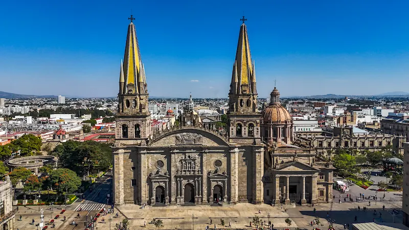 Vista aérea de la Catedral de Guadalajara con sus dos torres neogóticas amarillas y plaza circundante.