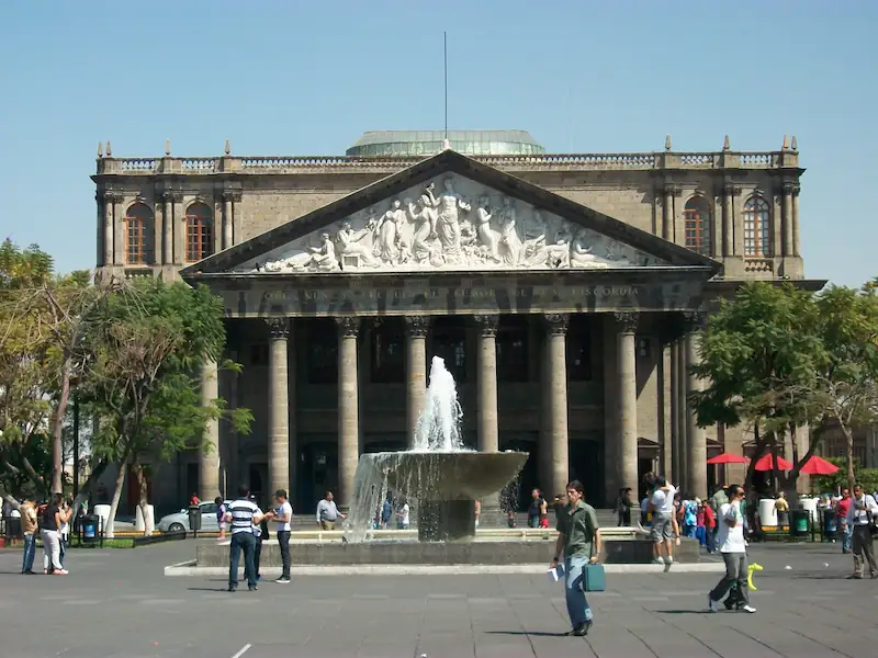 Fachada neoclásica del Teatro Degollado con columnas corintias y fuente de agua en la plaza frontal.