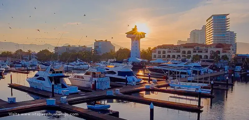 Embarcaciones y yates atracados en la Marina Ixtapa durante el atardecer con el faro al fondo.