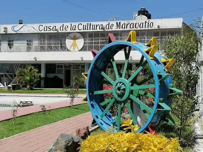 Fachada de la Casa de la Cultura de Maravatío con un gran timón o rueda agrícola decorativa de color azul en primer plano.