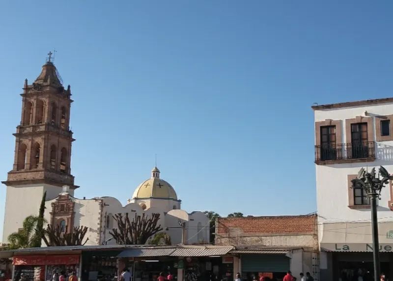 Torre del campanario de ladrillo y cúpula dorada de una iglesia en el centro histórico frente a locales comerciales.
