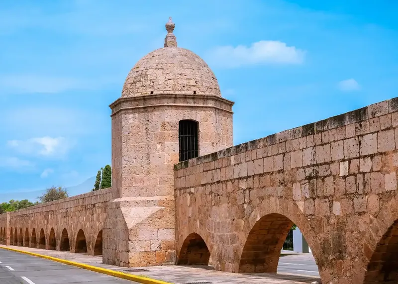 Arcos de cantera rosa del Acueducto de Morelia con su estructura colonial y una garita sobre la avenida.