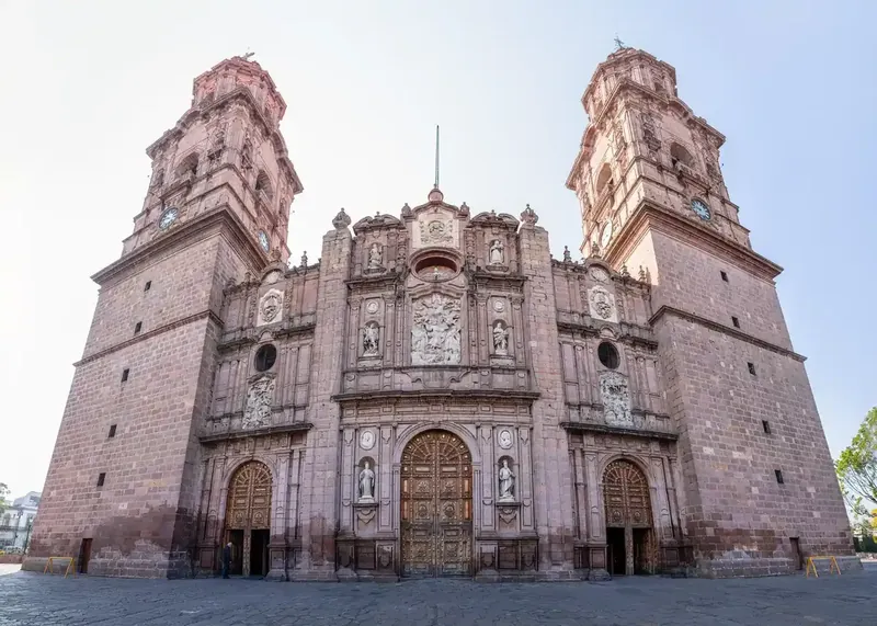 Fachada frontal y torres de la Catedral de Morelia en cantera rosa bajo un cielo claro.