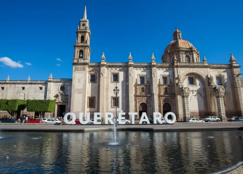 Letras monumentales de Querétaro frente al Templo de San Francisco y su espejo de agua bajo un cielo azul.