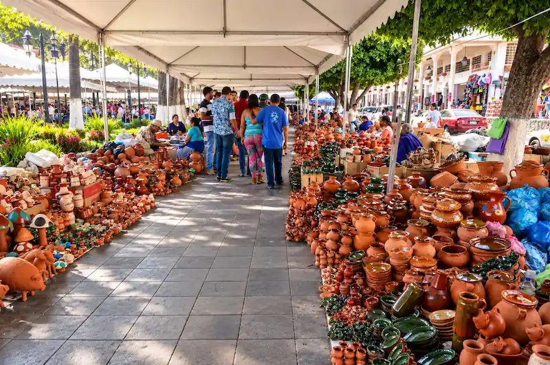 Pasillo del Tianguis Artesanal del Domingo de Ramos con puestos repletos de loza y artesanías de barro en Uruapan.