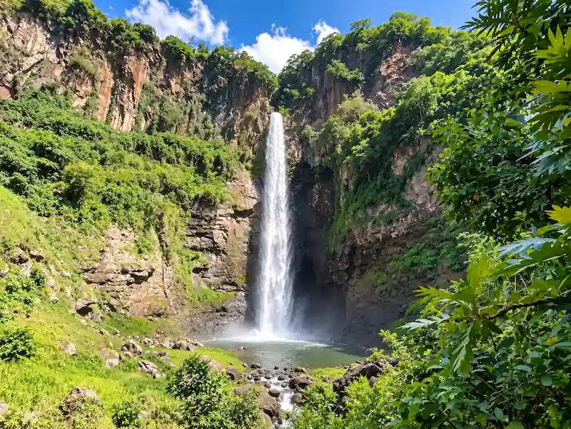 Impresionante caída de agua de la cascada de Curungueo rodeada de acantilados rocosos y densa vegetación verde.