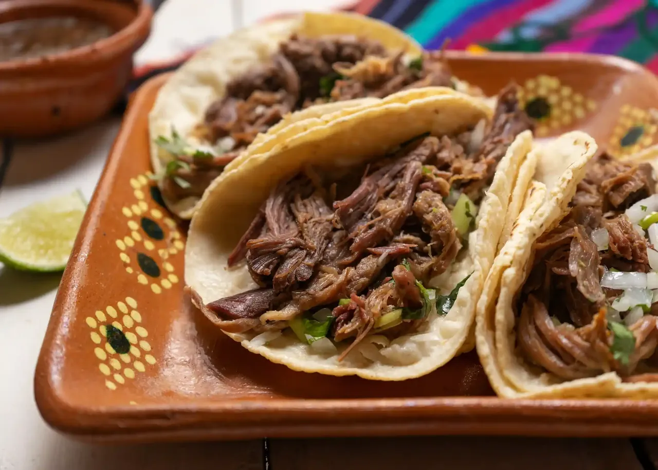 Tacos de barbacoa de borrego con cilantro y cebolla servidos en un plato de barro.