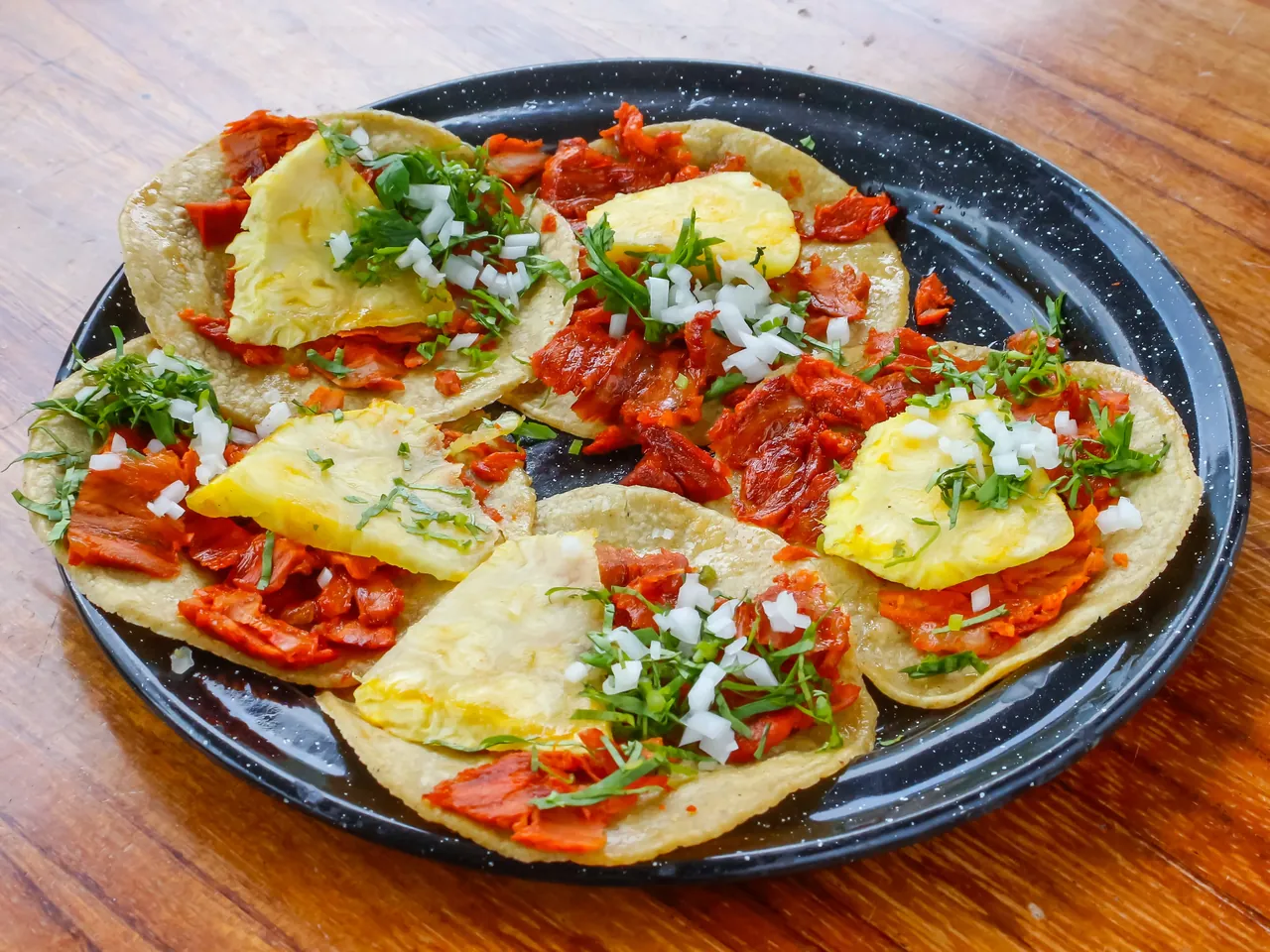 Plato con tacos al pastor preparados con carne adobada, piña, cebolla y cilantro.