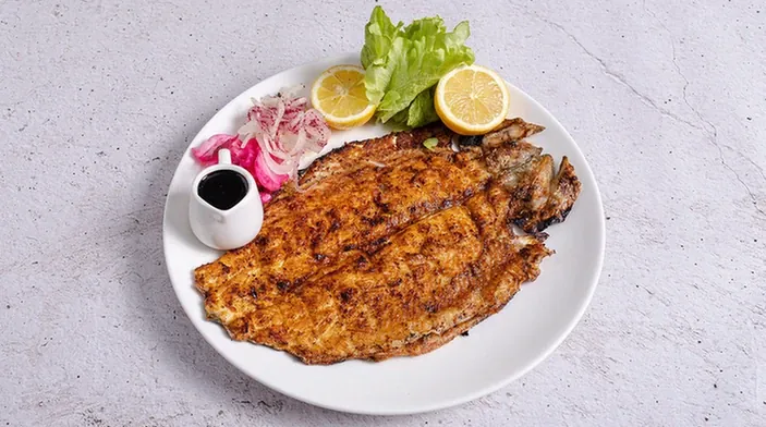Pescado a la talla a las brasas servido en un plato blanco con cebolla morada, ensalada y limones.