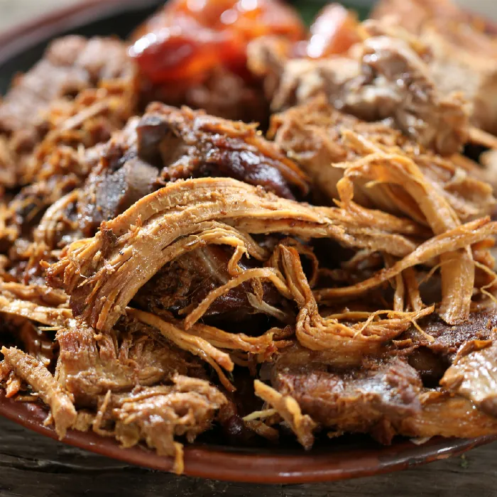 Plato hondo de barro servido con carnitas de cerdo michoacanas picadas y jugosas.