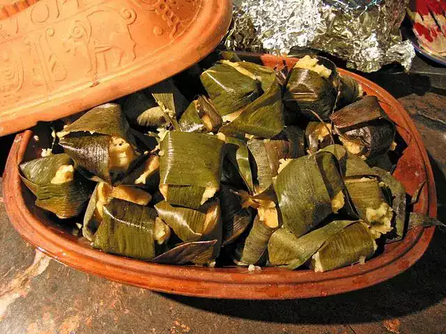 Cazuela de barro llena de corundas michoacanas envueltas en hojas verdes de planta de maíz.