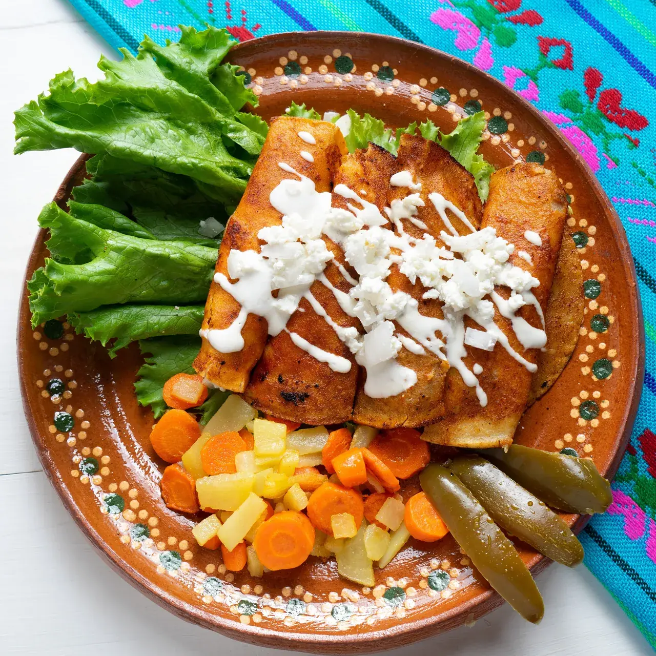 Plato de barro con enchiladas queretanas bañadas en crema y queso, acompañadas de papas, zanahorias y chiles en vinagre.
