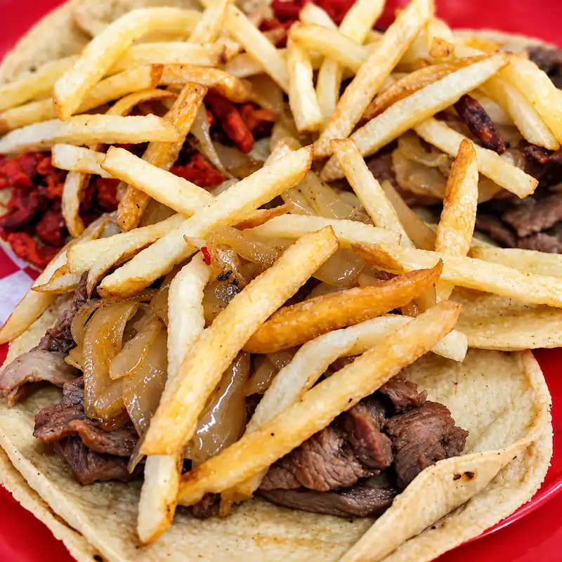 Tacos de cecina de res servidos con cebolla caramelizada y una generosa porción de papas a la francesa encima.