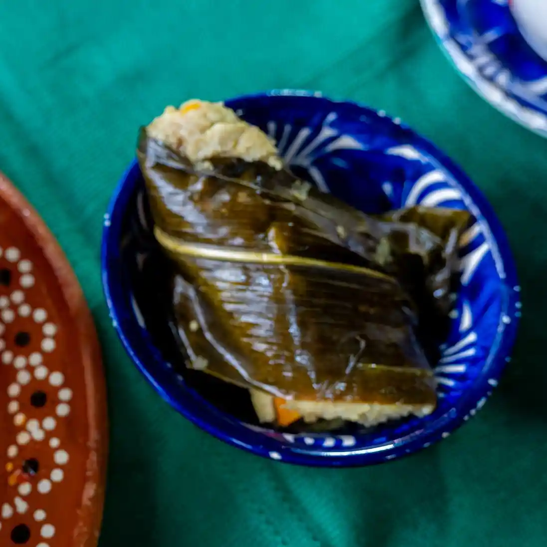 Corunda michoacana envuelta en hoja de maíz servida dentro de un tazón de cerámica azul.